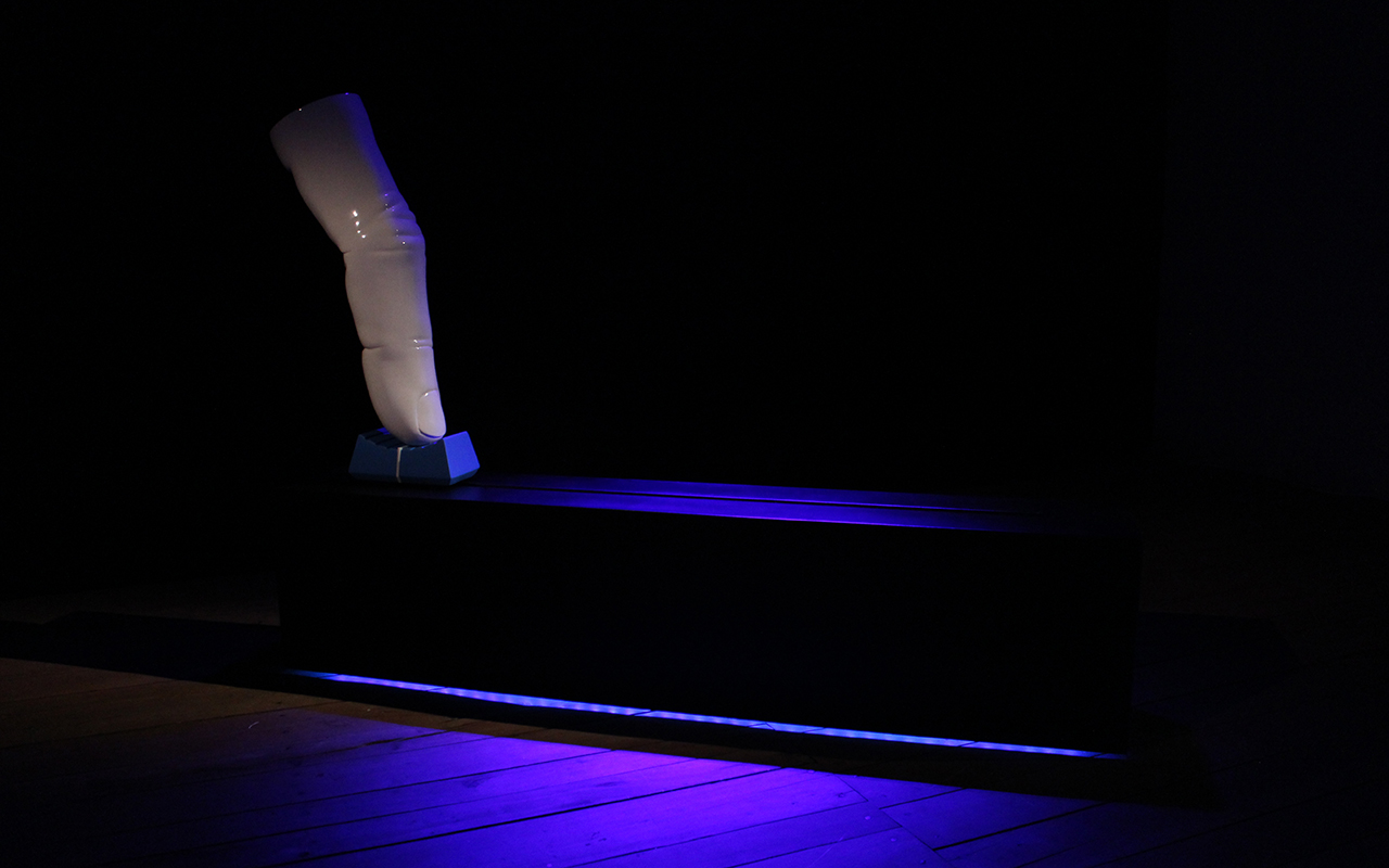 A big white finger with a porcellainic look sits on top of an oversizerd blue fader cap. Both are mounted on a large black box with faint, deep blue illumination.